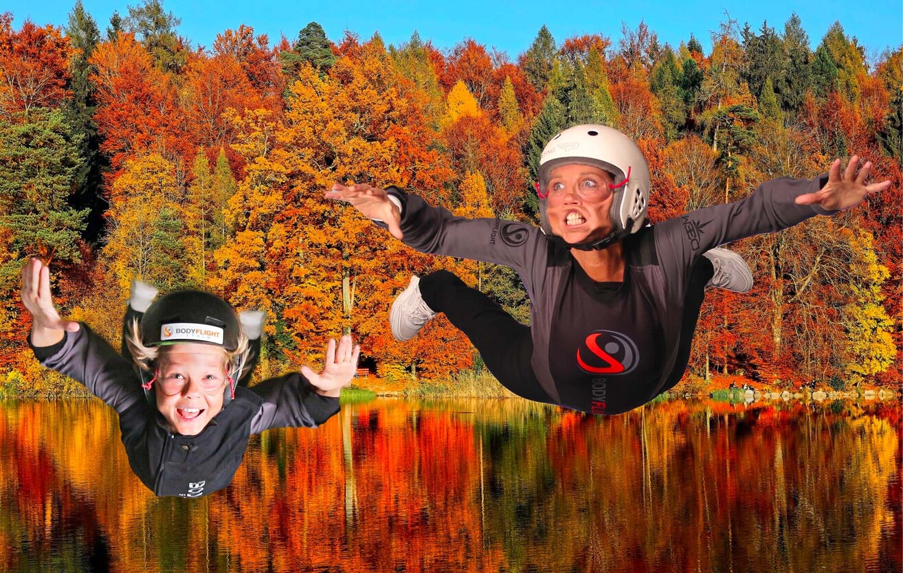 Barn och vuxen flyger ovanför vatten framför en höstskog. Bodyflight är en perfekt aktivitet att göra på höstlovet.